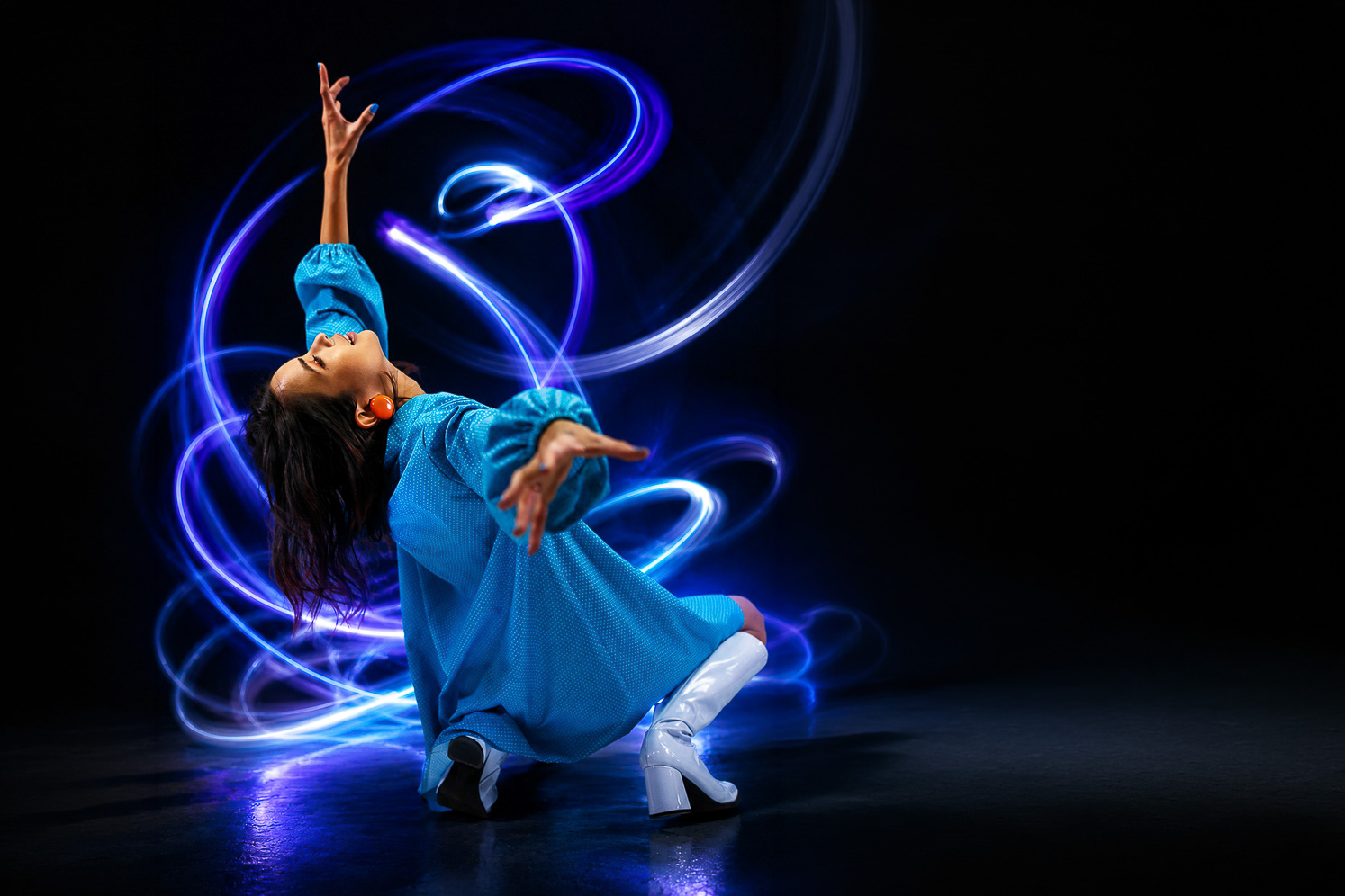 Light painting réalisé en longue exposition, sujet féminin en robe bleue entouré de traînées lumineuses bleues et violettes
