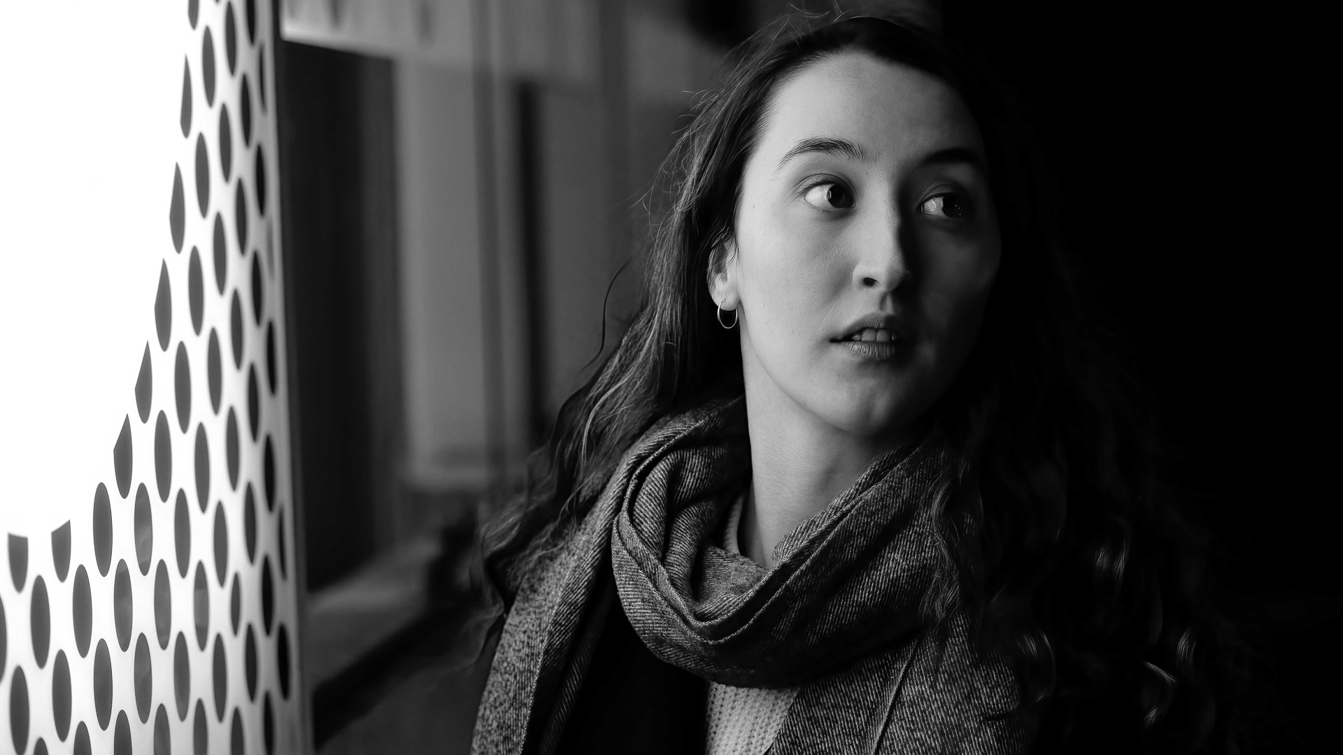 Portrait noir et blanc d'une femme éclairée latéralement par une enseigne lumineuse à motifs, environnement urbain